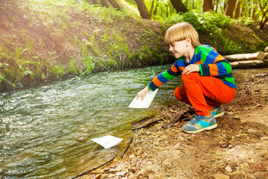 Little boy launching paper ships from riverside