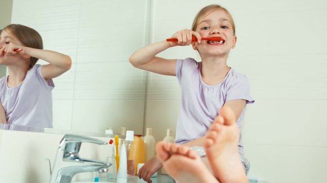 Portrait blonde child girl 7-8 years sitting in the bathroom and viewing her teeth and and uses the toothbrush. Zooming