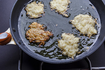 Frying latkes with raw side up and one turned in deep oil on pan on stove from above