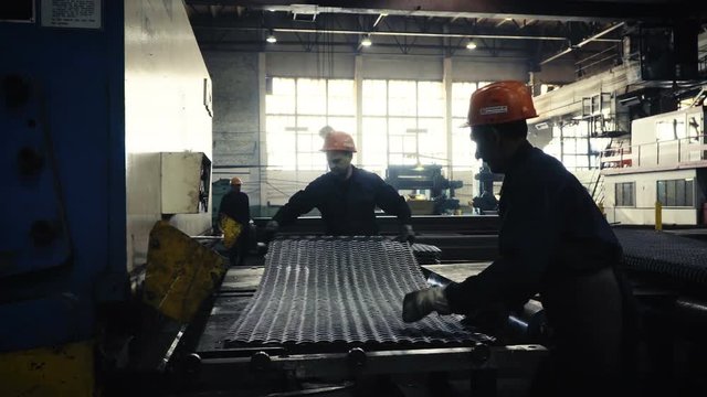 two workers of the plant or factory lift sheet metal. Cling and crane hooks are on the machine for cutting metal blade
