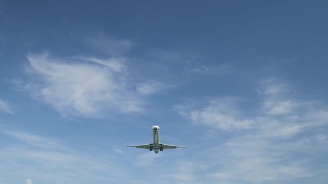 Airplane landing on island Bali airport under blue sea with waves on the horizon. Cinematic shot of overhead flying aircraft with beautiful ocean on cloudy sky background. Focal length 50 mm