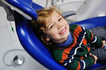 baby boy with curly red hair in blue dental chair. Children's dentist