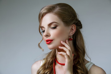 Beautiful woman with long wavy hair. She wear red earrings and beads on her neck. Red lips and golden eyelids makeup. Isolated on gray background.