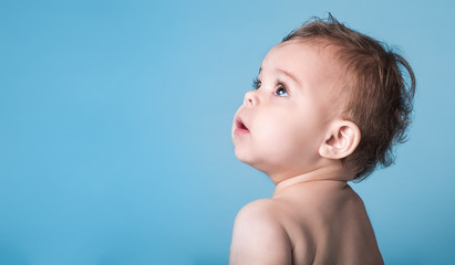 Cute Baby Girl Looking Up Against Vivid Blue Background - obrazy, fototapety, plakaty