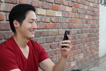 Portrait of a smiling Asian guy texting on mobile phone outside