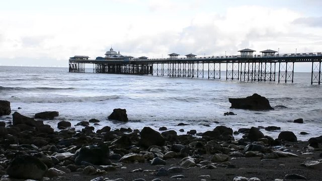LLandudno pier, seaside resort on North Wales coast, between Bangor and Colwyn bay. Victorian architecture. wide establishing shot with waves and the shore in foreground with rocks.