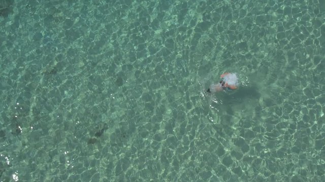 AERIAL: Man taking deep breath and swimming under sea surface towards wild beach