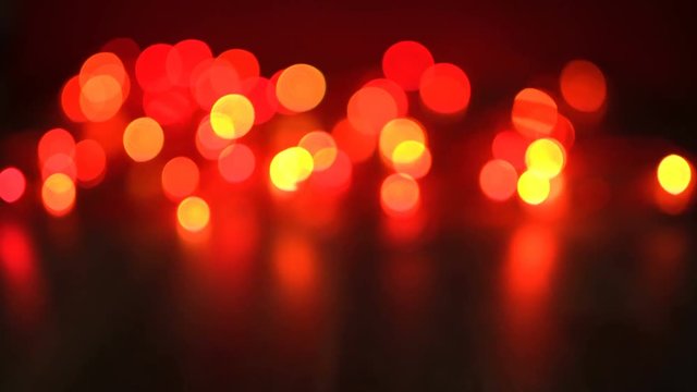 Defocused red Christmas lights on hardwood floor with reflection, glowing festive video background with seamless looping