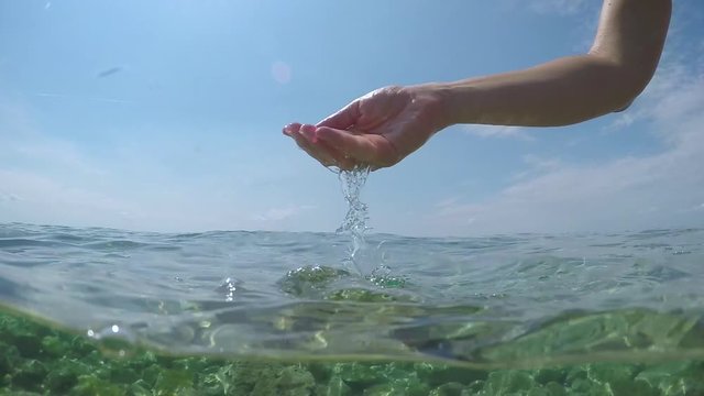 HALF UNDERWATER SLOW MOTION: Unrecognizable person scooping crystal clear water