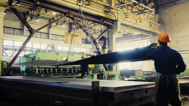 two workers of the plant or factory lift sheet metal. Cling and crane hooks are on the machine for cutting metal blade