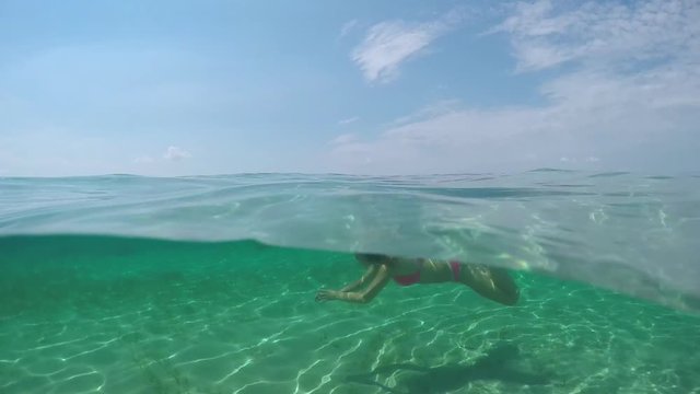 UNDERWATER: Happy young woman swimming underwater and exploring amazing ocean