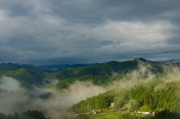 Mountain forest with fog against dramatic sky on the background