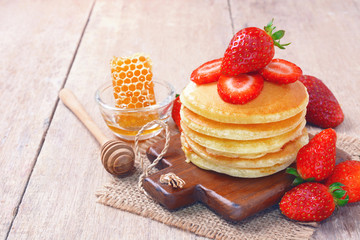 Delicious pancake with fresh strawberry on top with honeycombs in glass bowl on wooden background, Stack of pancakes on the table.