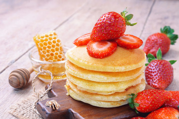 Delicious pancake with fresh strawberry on top with honeycombs in glass bowl on wooden background, Stack of pancakes on the table.