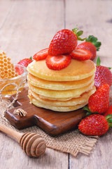 Delicious pancake with fresh strawberry on top with honeycombs in glass bowl on wooden background, Stack of pancakes on the table.