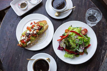 Useful lunch, plate with leaves of a splpt, a sandwich with avocado sauce and tomatoes and black coffee.