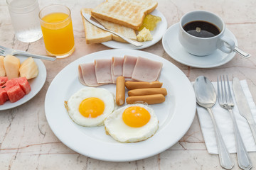 Breakfast with Fried egg, Ham, Sausage, toast, jam, butter, water melon, orange juice and black coffee on marble table.