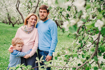 spring portrait of happy family enjoying holidays in blooming garden. Pregnant mother, father and son walking together outdoor