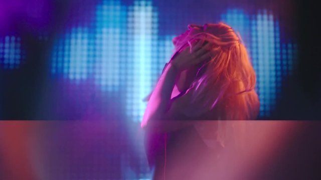 Blond female DJ jumping, singing and dancing behind decks on party in nightclub