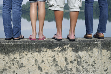 legs of teens standing on wall near lake