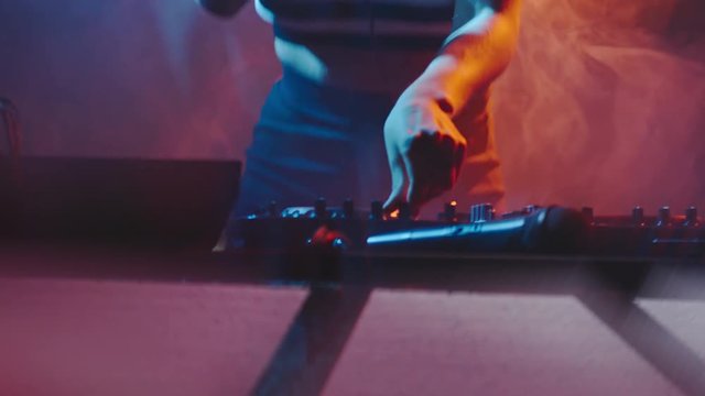 Blond female DJ listening to song in headphones and playing set at party in nightclub