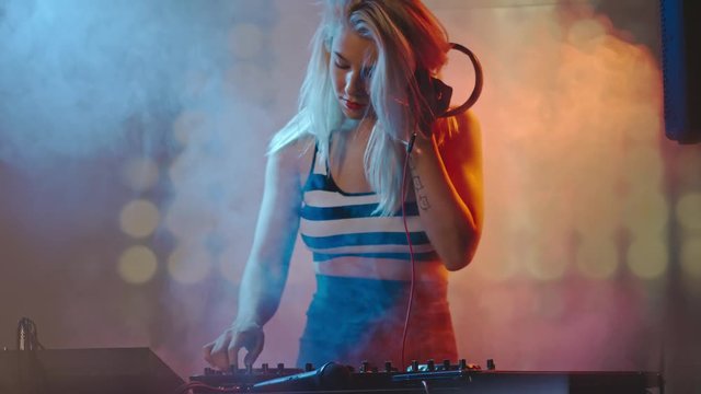 Seductive blond woman dancing and DJing in smoky nightclub