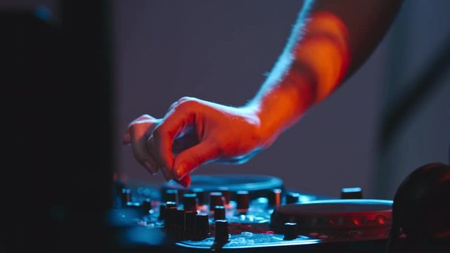 Hands of dancing female DJ turning knobs on professional mixer console and playing music in nightclub 