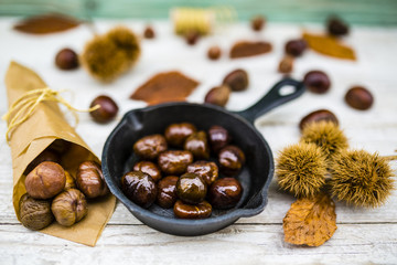 Delicious and hot roasted chestnuts on frying pan on old wooden background. Tasty street food. 