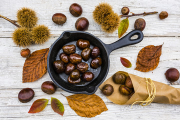 Delicious and hot roasted chestnuts on frying pan on old wooden background. Tasty street food. 