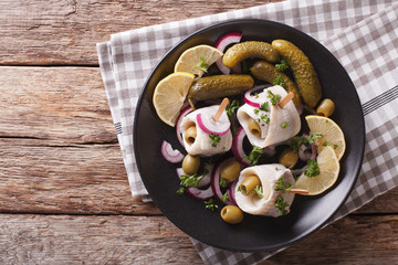 rolls of marinated herring with olives, onions, pickles and lemon close-up on a plate. horizontal top view