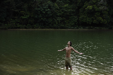 Young man standing in lake, arms open wide