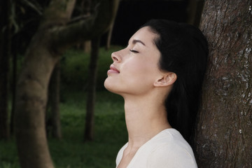 Young woman leaning against tree trunk