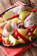 salad of herring with potatoes, green apple, onion, pepper and olives macro on a plate. Vertical