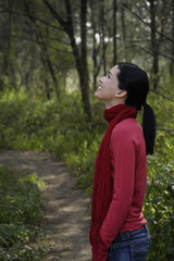 Young woman on wooded path looking up into trees