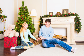 Nice love couple sitting on carpet near the fireplace. Woman and man celebrating Christmas