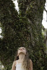 Naklejka premium young girl looking up to sky, standing by tree