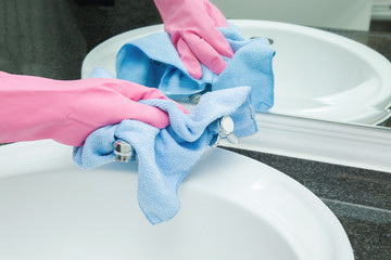 Maid or housewife washing and polishing marble surface, ceramic sink and water tap in the bathroom. House and hotel cleaning. General cleaning or regular wash.