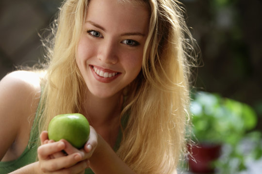 head shot of young woman holding green apple