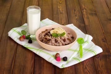 Bowl porridge, glass milk, spoon, nuts, towel on dark wooden.