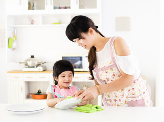 little girl helping her mother clean dish in the kitchen