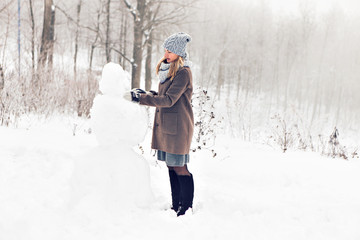 Fototapeta na wymiar Woman making a snowman in winter time