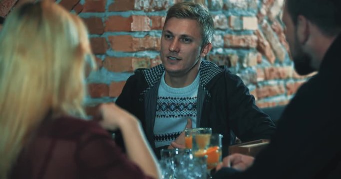 Friends talking at bar 4k video. Young man laughing at cafe table with beverage, people having a good time together and gossiping