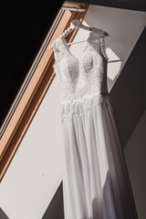 White Wedding dress hang on a shoulders near window, before ceremony