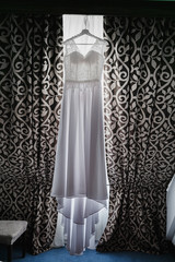 White Wedding dress hang on a shoulders near window, before ceremony