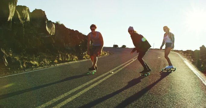 Skateboarders bombing down steep hill at sunset