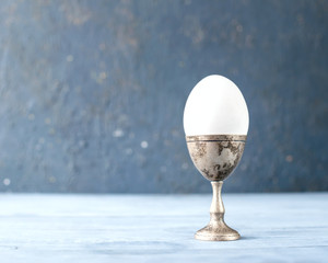 White fresh egg on a metal stand on the grey background.