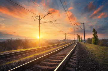 Railway station against beautiful sky at sunset. Industrial landscape with railroad, colorful blue sky with red clouds, sun, trees and green grass. Railway junction. Heavy industry. Evening in autumn