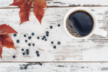 Black tea in white porcelain cup on wooden table with leaves and berries of wild grapes