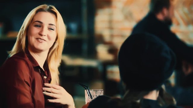 Young beautiful woman talking smiling man at bar HD slow motion video. Couple sitting in cafe with beverage cocktails, blonde girl flirts with guy