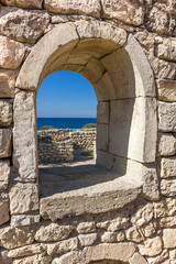 Fototapeta na wymiar ancient stone wall with a semicircular window and a view of the